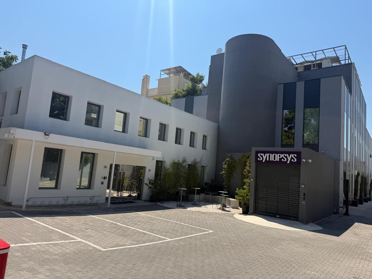 Both wings across the parking court — the white block, and the glazed offices behind the drum.